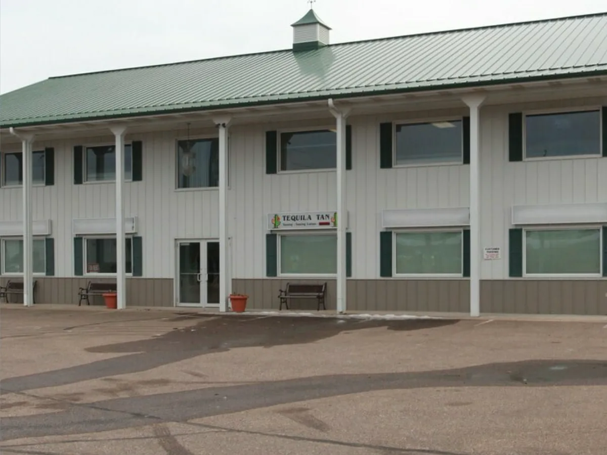 Two-story office and retail building with a green metal roof and cupola beside a large paved lot near I-94 and State Hwy 12-29, Wisconsin